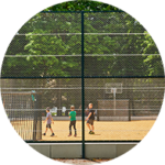 Blick von außen auf die Stirnseite eines Ballfangzauns, im Hintergrund spielende Kinder.